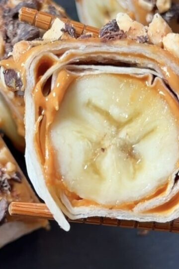 Homemade banana dessert sushi sliced into bite-sized rolls with peanut butter, chopped peanuts, and chocolate chips.
